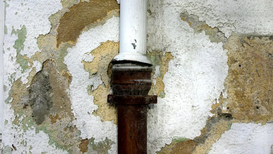 Corroded pipe running through a wall with peeling, water-stained plaster